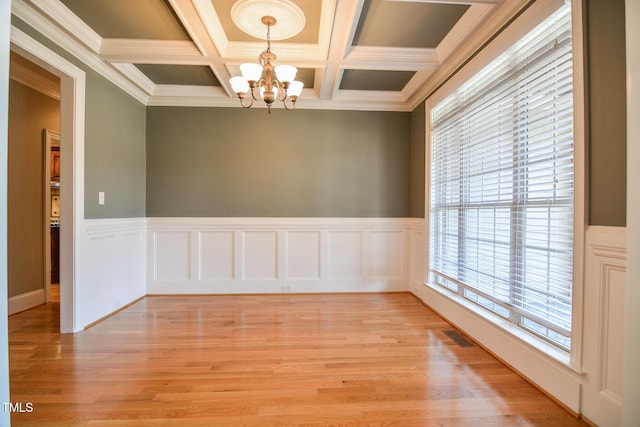 spare room with a chandelier, coffered ceiling, visible vents, light wood-style floors, and beamed ceiling