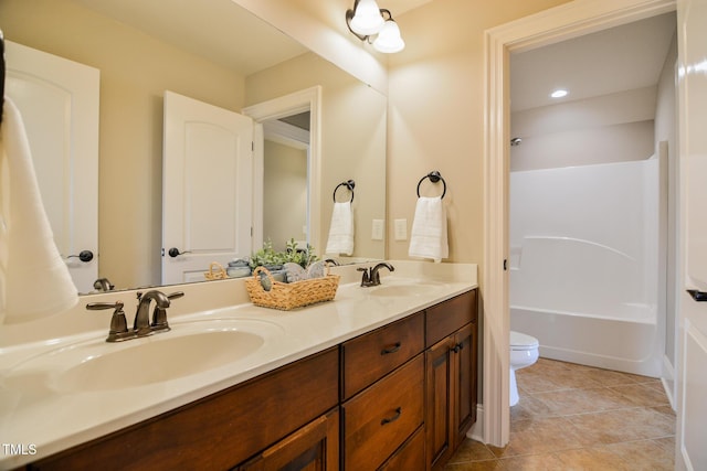 full bath with toilet, double vanity, a sink, and tile patterned floors