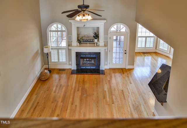 unfurnished living room featuring visible vents, a high end fireplace, ceiling fan, wood finished floors, and baseboards