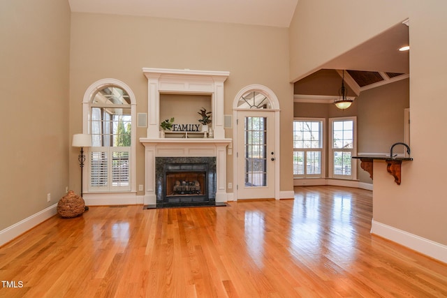 unfurnished living room with a towering ceiling, a fireplace, baseboards, and wood finished floors