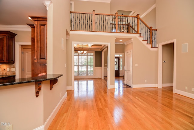 unfurnished living room with ornamental molding, stairway, a high ceiling, light wood-style floors, and a chandelier