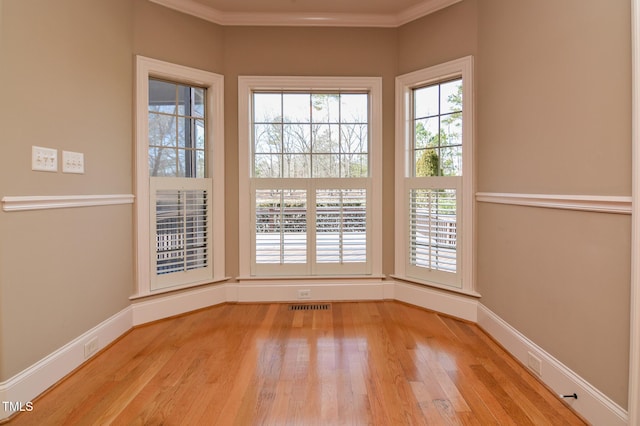 spare room with baseboards, visible vents, wood finished floors, and ornamental molding