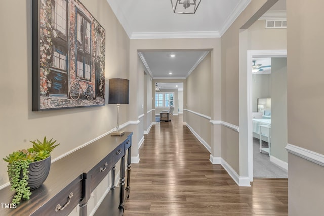 hallway featuring visible vents, baseboards, dark wood-style flooring, and crown molding