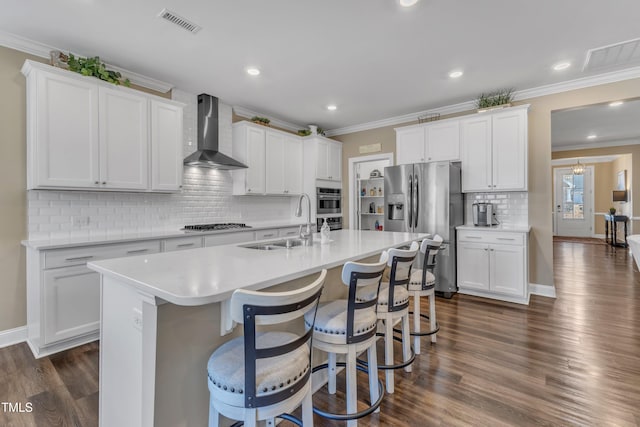 kitchen with a sink, wall chimney range hood, ornamental molding, and stainless steel appliances