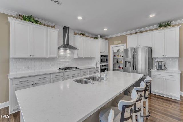 kitchen with a sink, stainless steel appliances, crown molding, and wall chimney range hood