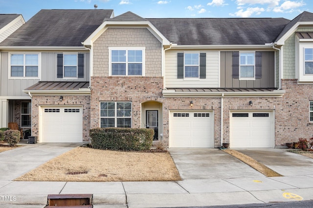 multi unit property featuring a garage, a standing seam roof, and brick siding