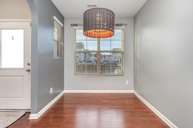 unfurnished dining area with arched walkways, wood finished floors, visible vents, and baseboards