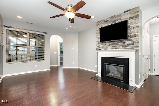 unfurnished living room with arched walkways, a stone fireplace, wood finished floors, and baseboards