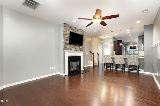 unfurnished living room with dark wood-style floors, a large fireplace, visible vents, and a ceiling fan