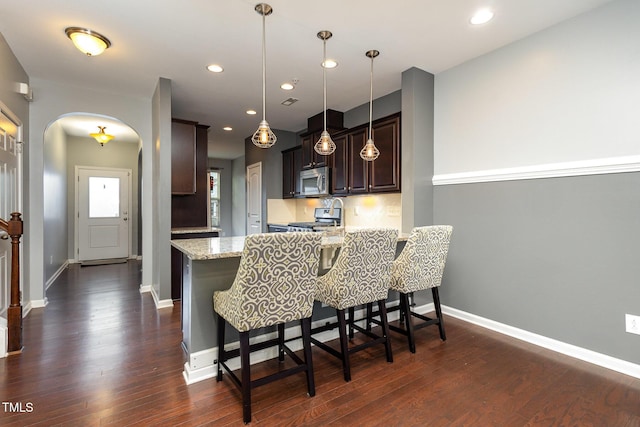 kitchen featuring arched walkways, stainless steel appliances, a peninsula, dark wood-style flooring, and a kitchen bar