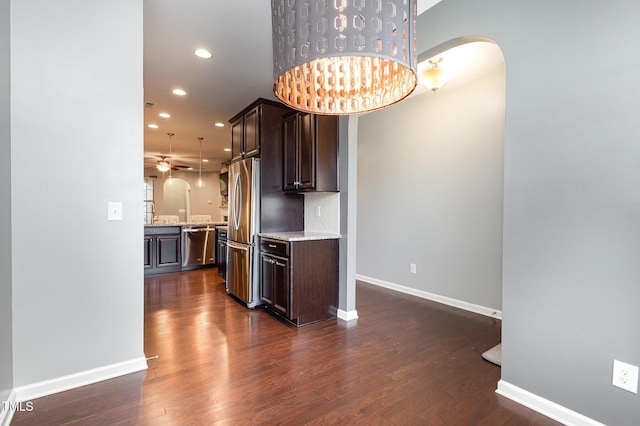 kitchen featuring arched walkways, stainless steel appliances, dark brown cabinets, and dark wood-type flooring