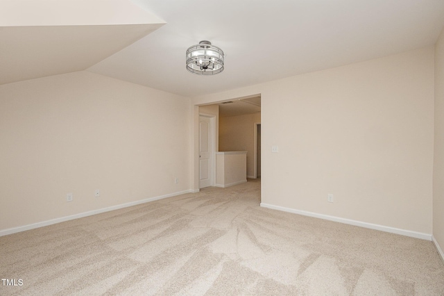 spare room with light carpet, vaulted ceiling, and baseboards