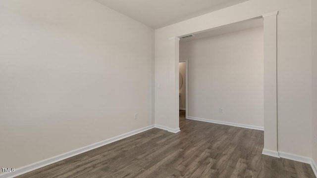 unfurnished room with dark wood-style flooring, visible vents, and baseboards