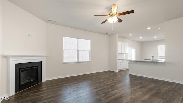 unfurnished living room with dark wood-style flooring, visible vents, and a healthy amount of sunlight