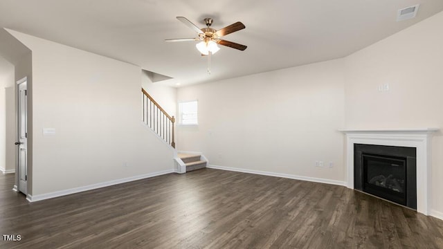 unfurnished living room featuring dark wood finished floors, stairway, a ceiling fan, a glass covered fireplace, and baseboards