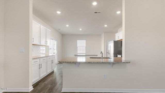 kitchen featuring light stone counters, a kitchen breakfast bar, freestanding refrigerator, white cabinetry, and a sink