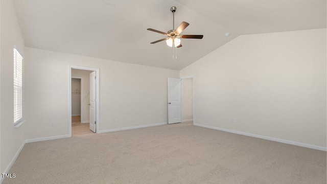 empty room featuring light carpet, a ceiling fan, baseboards, vaulted ceiling, and plenty of natural light