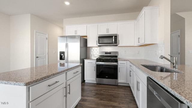 kitchen with stainless steel appliances, tasteful backsplash, white cabinets, a sink, and light stone countertops