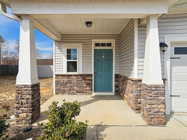 entrance to property featuring stone siding, fence, and covered porch