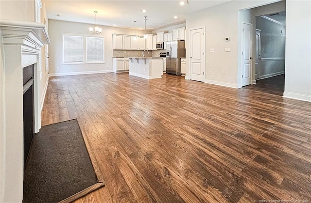 unfurnished living room with a notable chandelier, recessed lighting, dark wood-type flooring, a fireplace with flush hearth, and baseboards