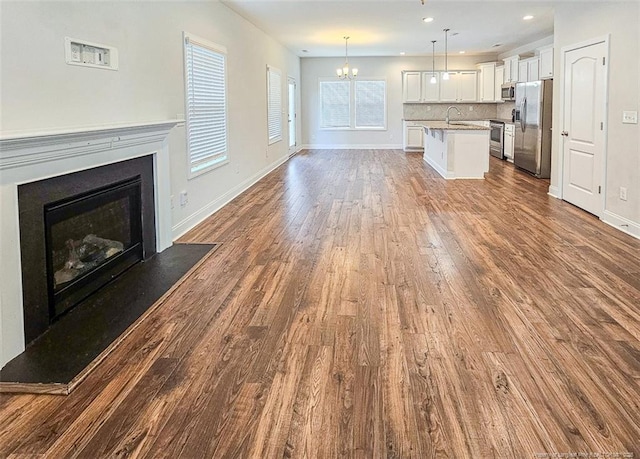 unfurnished living room with a chandelier, dark wood-style flooring, a fireplace with raised hearth, and baseboards