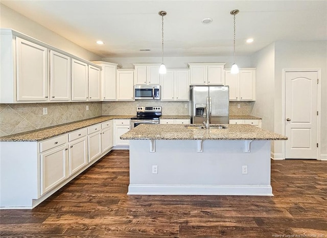 kitchen with appliances with stainless steel finishes, a kitchen island with sink, dark wood finished floors, and light stone countertops