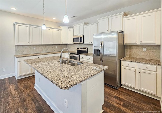 kitchen with a center island with sink, dark wood-style flooring, light stone countertops, stainless steel appliances, and a sink