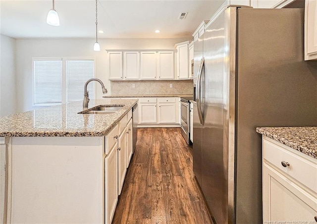 kitchen with a sink, appliances with stainless steel finishes, decorative backsplash, an island with sink, and dark wood finished floors