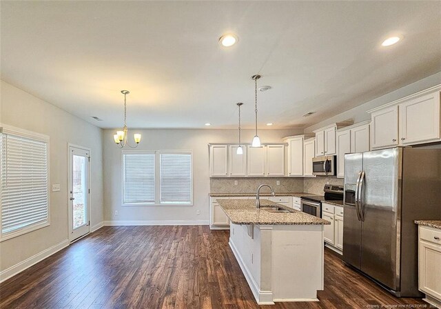 kitchen featuring light stone counters, dark wood-type flooring, a sink, appliances with stainless steel finishes, and backsplash