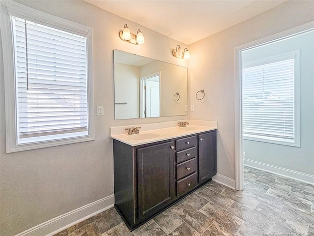 bathroom featuring double vanity, stone finish flooring, baseboards, and a sink