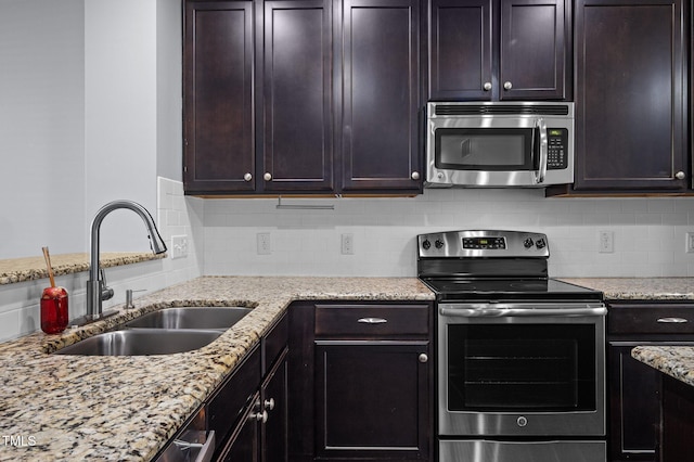 kitchen with light stone counters, backsplash, appliances with stainless steel finishes, dark brown cabinetry, and a sink