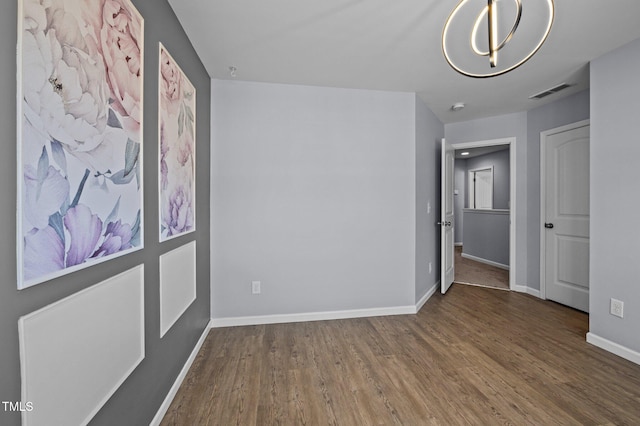 unfurnished bedroom featuring an inviting chandelier, wood finished floors, visible vents, and baseboards