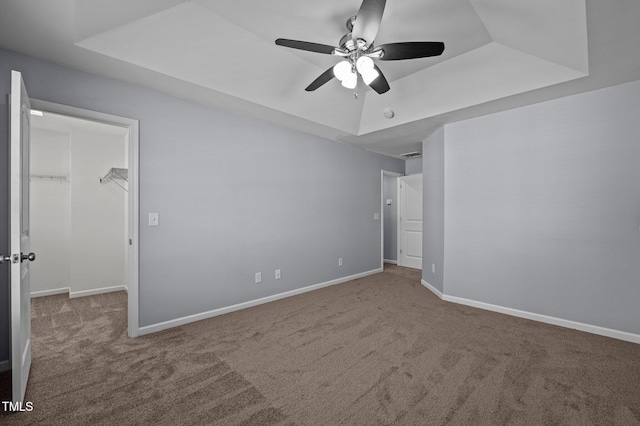 unfurnished bedroom featuring a walk in closet, baseboards, and a raised ceiling