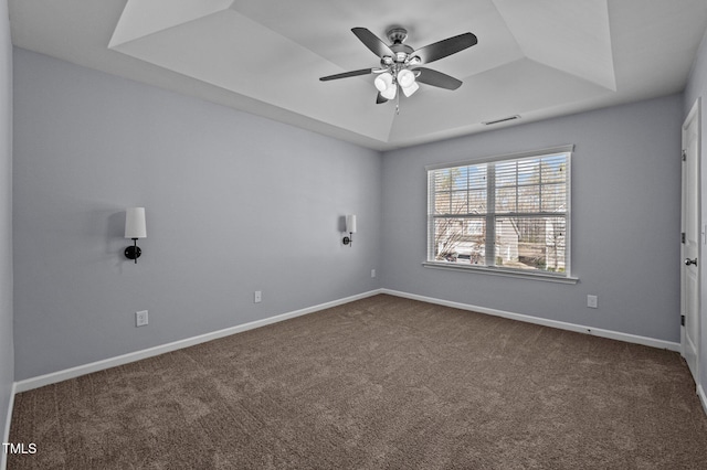 empty room featuring dark colored carpet, a raised ceiling, visible vents, a ceiling fan, and baseboards