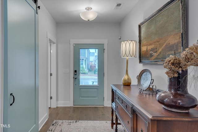 foyer entrance with a barn door, wood finished floors, and visible vents