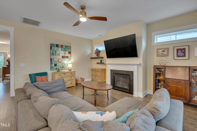 living room featuring visible vents, baseboards, a ceiling fan, light wood finished floors, and a glass covered fireplace