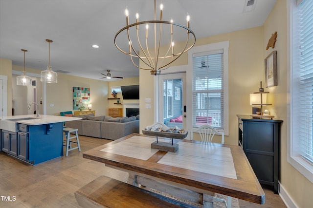 dining room featuring a fireplace, visible vents, light wood-type flooring, baseboards, and ceiling fan with notable chandelier