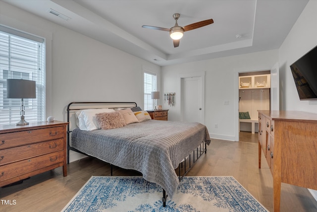 bedroom featuring light wood-style floors, visible vents, a tray ceiling, and baseboards