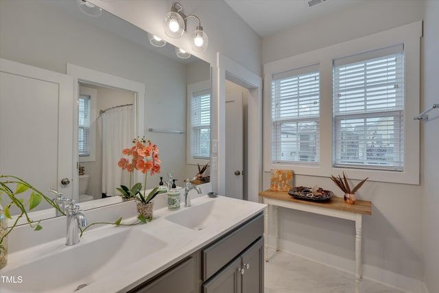 bathroom featuring marble finish floor, a sink, toilet, and double vanity