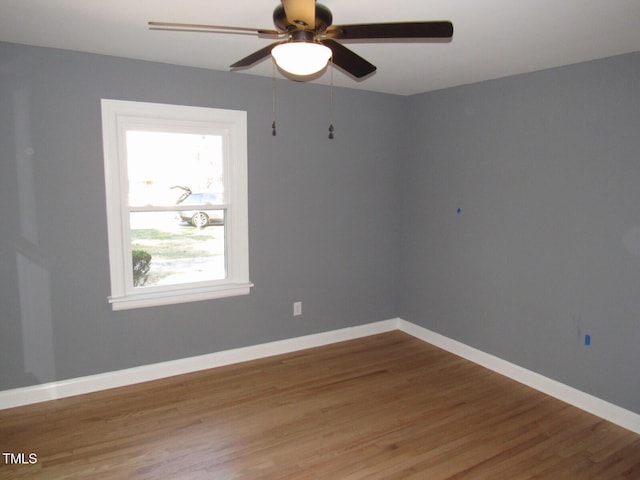 empty room with wood finished floors, a ceiling fan, and baseboards