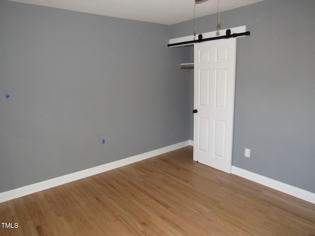 spare room featuring light wood-type flooring, a barn door, and baseboards