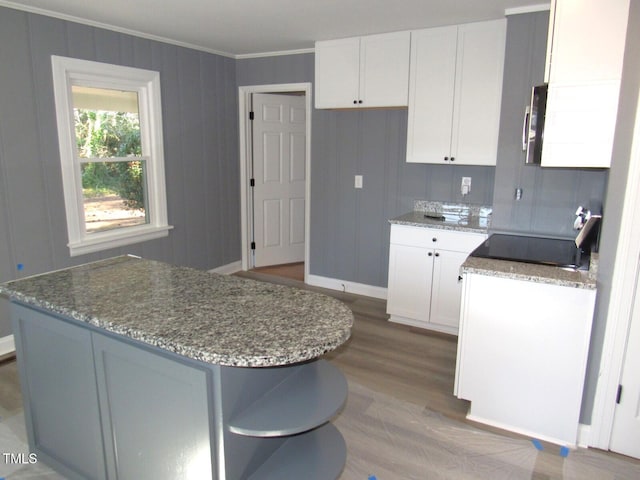 kitchen featuring ornamental molding, light stone counters, stainless steel microwave, light wood-type flooring, and white cabinetry