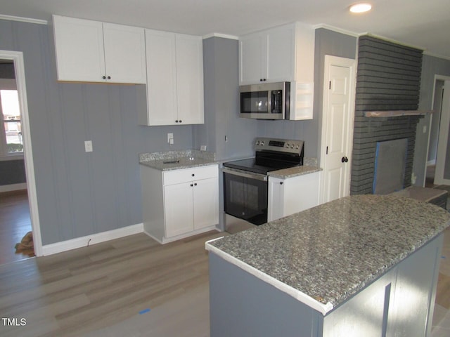 kitchen featuring light stone counters, light wood-style flooring, white cabinetry, appliances with stainless steel finishes, and a brick fireplace