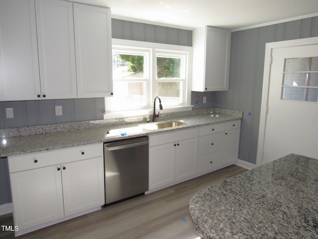 kitchen featuring light wood finished floors, light stone counters, stainless steel dishwasher, white cabinetry, and a sink