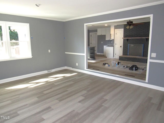 interior space featuring a fireplace, a ceiling fan, baseboards, light wood-type flooring, and crown molding