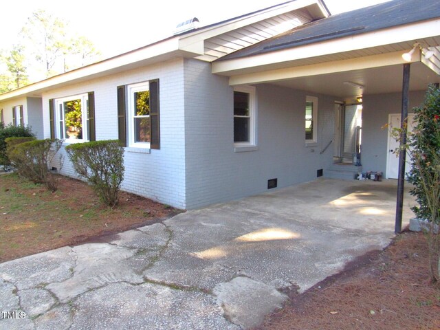 view of side of property with brick siding, crawl space, and an attached carport