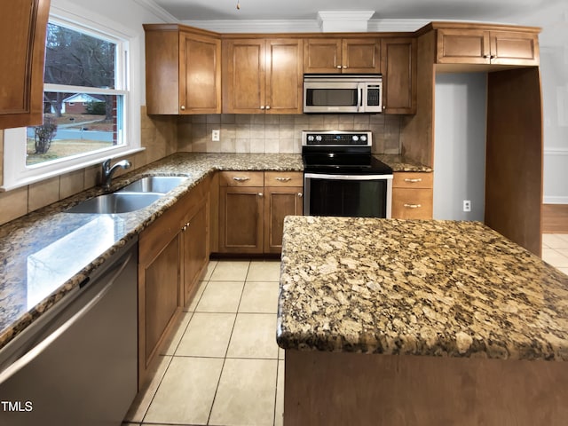 kitchen featuring stone counters, a sink, appliances with stainless steel finishes, backsplash, and brown cabinets