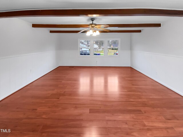 empty room featuring beam ceiling, wainscoting, ceiling fan, and wood finished floors