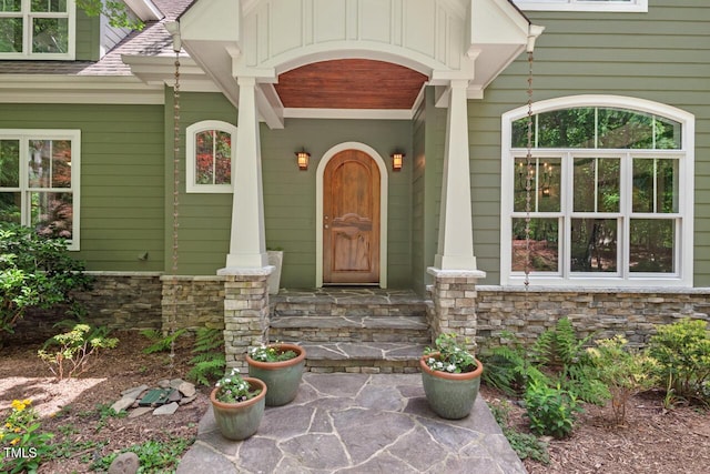 doorway to property with stone siding, roof with shingles, and covered porch