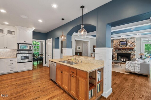 kitchen featuring stainless steel appliances, a sink, light wood-style flooring, a fireplace, and recessed lighting